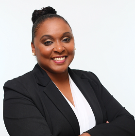 A professional woman with a warm smile, wearing a black blazer over a white blouse, stands confidently with her arms crossed against a plain white background.