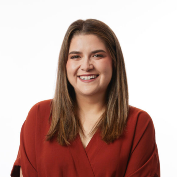 A woman with long, straight brown hair is smiling, wearing a deep red blouse, against a white background.