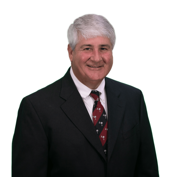 A middle-aged man with short gray hair, wearing a black suit and a white dress shirt, along with a maroon tie featuring a pattern of small icons. He is smiling and facing forward against a white background.