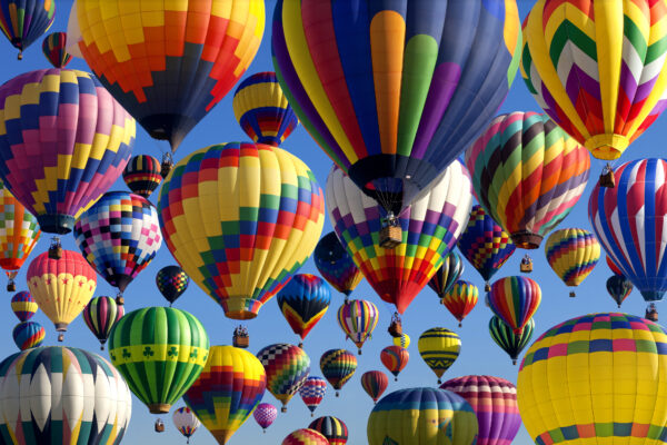 An array of colorful hot air balloons in various patterns and designs floating against a clear blue sky.