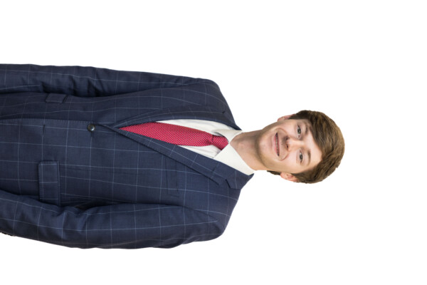 A young man in a navy blue checkered suit and a red tie, standing and smiling against a white background.