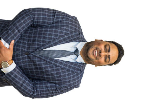 A smiling man wearing a blue plaid suit and a light blue shirt, standing with his arms crossed.