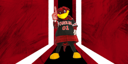 A cartoon mascot dressed in a black jersey with garnet and white accents and the word 'CAROLINA' is holding a foam finger that says 'GAMECOCKS'. The background features bold garnet and white graphic elements.