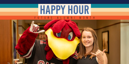 A person poses with a large, animated bird mascot wearing a dark jersey. The person is smiling and making a hand gesture, surrounded by a colorful banner reading "HAPPY HOUR FUTURE ALUMNI MONTH".