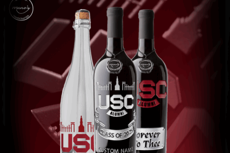 Three wine bottles with custom labels featuring university-themed designs. The left bottle is clear with 'USC' printed in red; the center bottle is dark with 'USC ALUMNI' and 'Class of 2025' inscriptions, and a black bottle on the right reads 'Forever to Thee' with 'SC' in red. The backdrop is a deep maroon color.