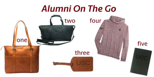 A collection of USC alumni merchandise including a brown leather tote, a black duffel bag, a luggage tag, a pink hoodie, and a green notebook.
