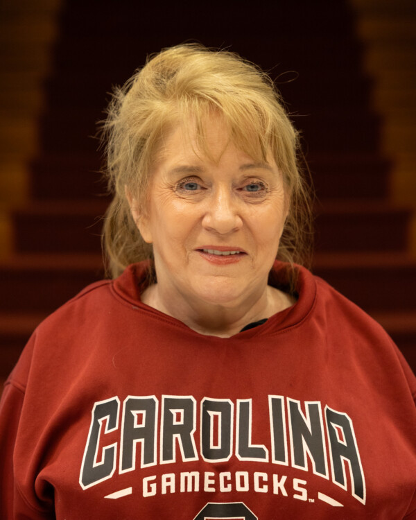 A woman with blonde hair wearing a red sweatshirt featuring the text "Carolina Gamecocks" is smiling.