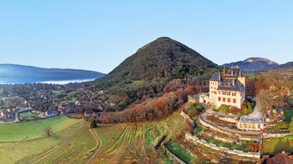 A scenic view of a castle on a hillside, surrounded by lush green fields and mountains in the background.