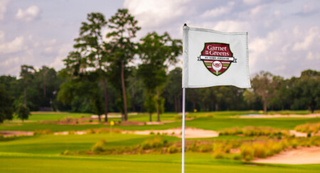 A white golf flag with a crest design, featuring "Garnet & Greens" and "USC," set against a lush green golf course backdrop.