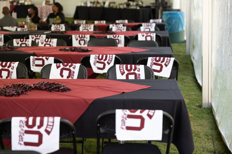 Tables set for an event, featuring maroon and black tablecloths, with decorative napkins displaying "50" on each chair.