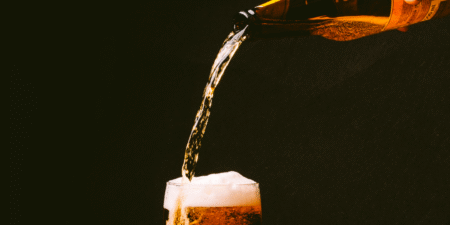 A bottle pours beer into a glass, creating a frothy head against a dark background.