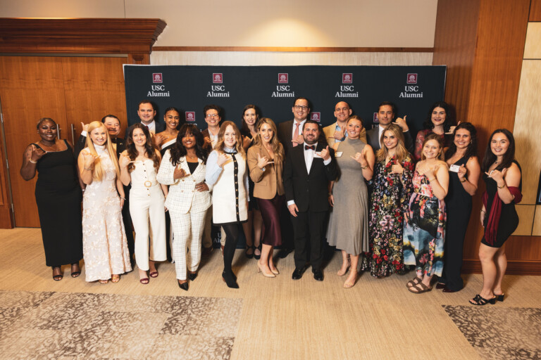A diverse group of alumni posing together at a USC Alumni event, showcasing a mix of formal and semi-formal attire.