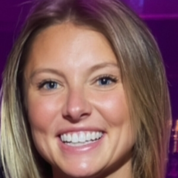 A smiling woman with long blonde hair wearing a black top, set against a vibrant, colorful background.