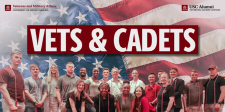 A group of diverse individuals posing together with a large American flag in the background, displaying "VETS & CADETS" prominently.