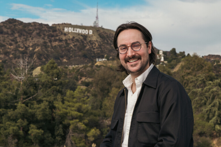 Man with glasses smiling with Hollywood sign and mountains in background